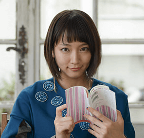 吉岡里帆が青い服を着て本を開いて見ている画像